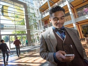 Young Black man in tweed jacket and bowtie checking phone in lobby of Lundquist College of Business