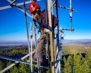 young man in hardhat stands high above treetops in wildfire observation tower