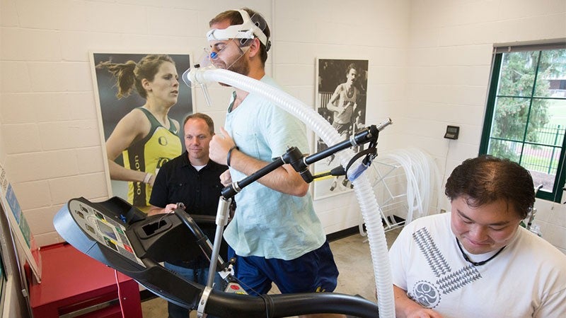 A professor working with a subject wearing an oxygen mask while running on a treadmill