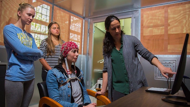 Two students and a professor with a subject wearing a cap with electrodes