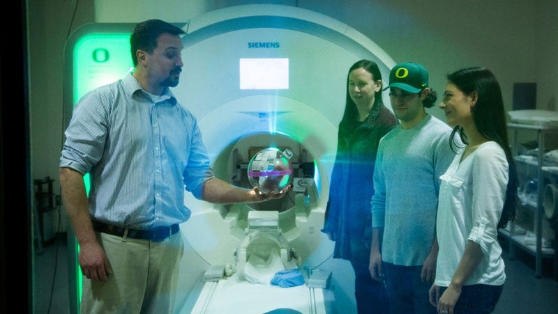 A professor talking to students at an MRI machine