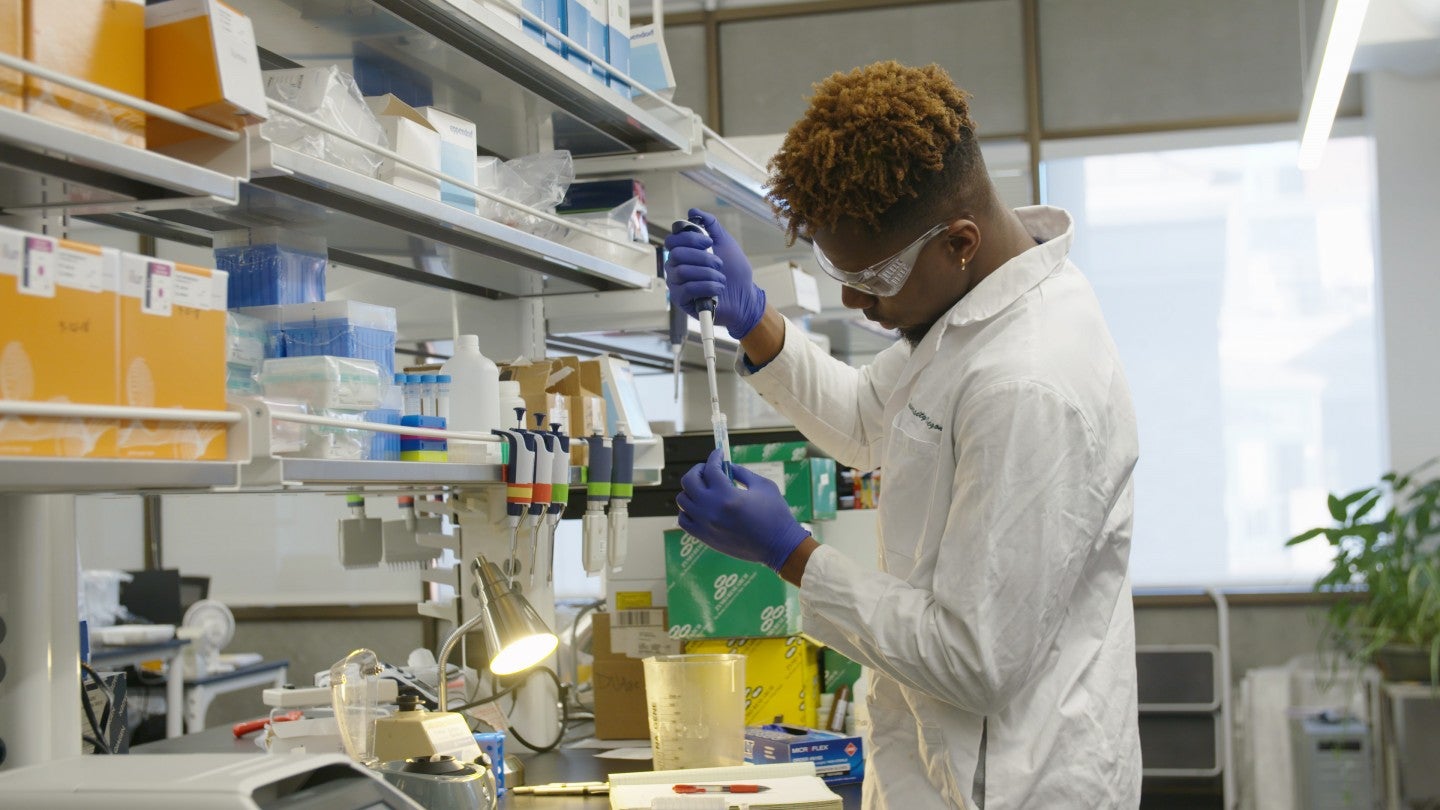 Student working in lab wearing white coat, safety goggles, and gloves