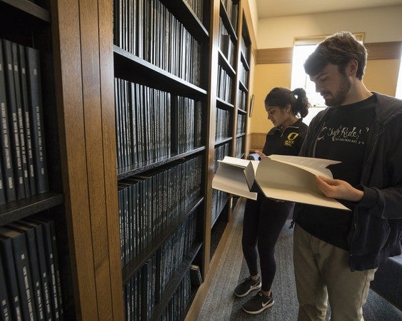 young man and woman examine bound volumes of theses prepared by previous Clark Honors College students