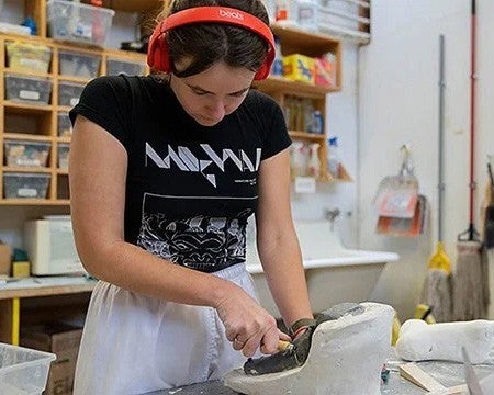 young woman wearing headphones sculpting object on tabletop