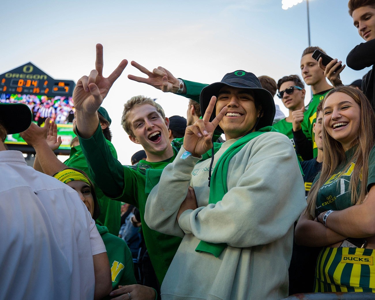 Students in Autzen Stadium stands making victory signs with fingers.