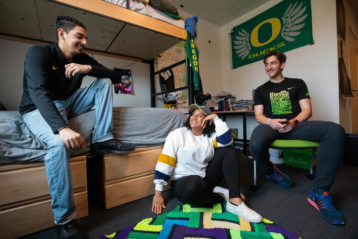 Two male, one female student socializing iin a dorm room.