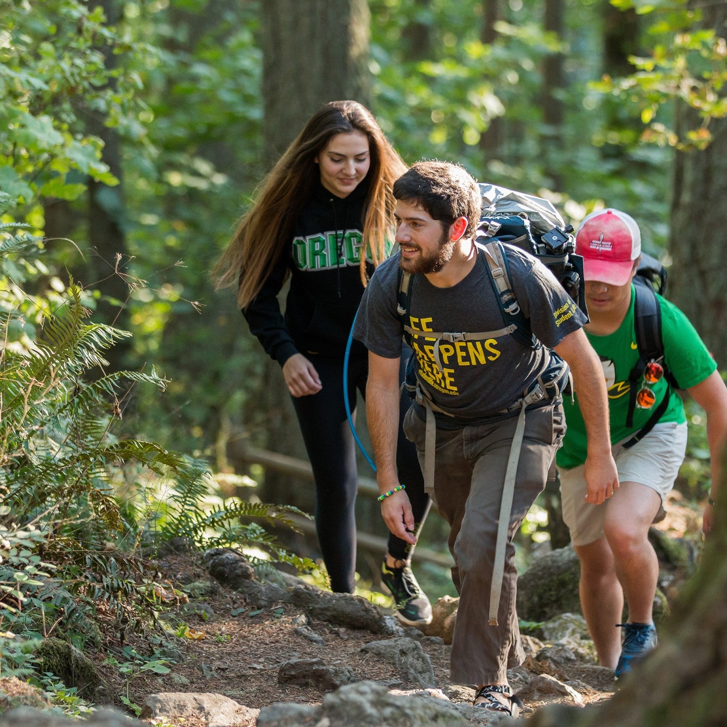 Two male, one female students hiking on forest trail.