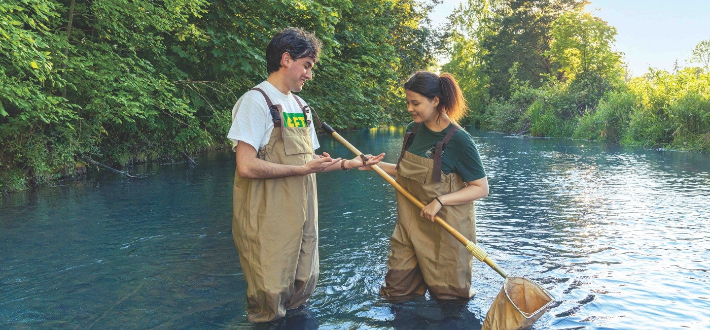 Male professor and female student examine an organism they've netted while surveying a river.