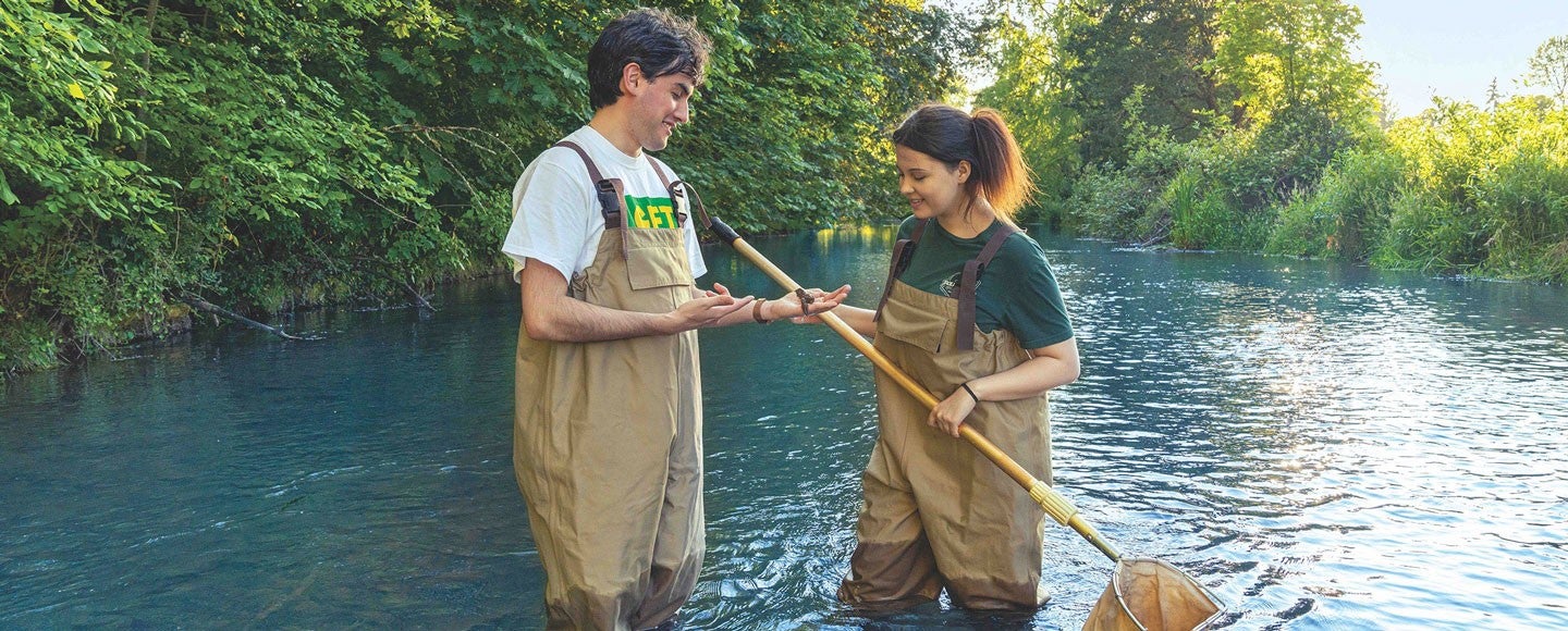 students in a river in waders with a net for course-related activity