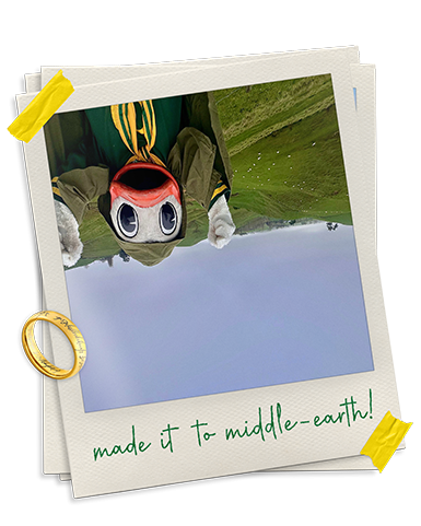 Upside down photo of the Oregon Duck wearing a cloak from the Lord of the Rings movies, with rolling green hills behind him