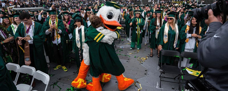 The Duck embracing a student wearing duck feet at UO commencement