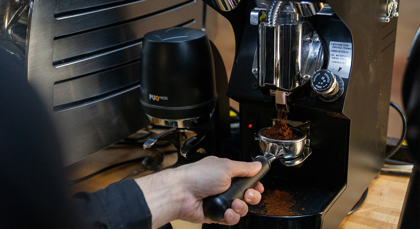 a person grinding coffee into a portafilter using an espresso grinder