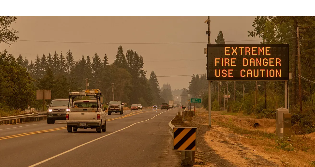 a digital sign next to a highway on a smoky day reads "Extreme fire danger use caution"