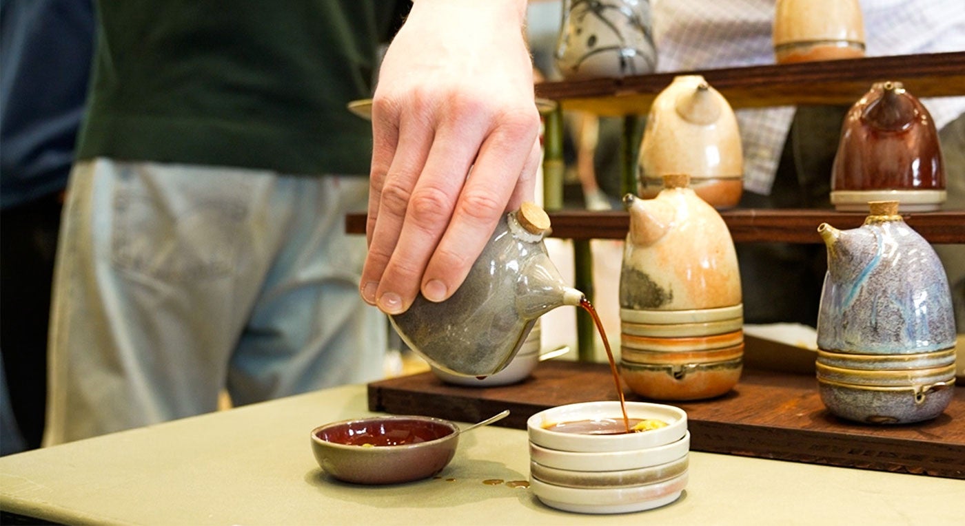 a person pours soy sauce from a handmade ceramic vessel