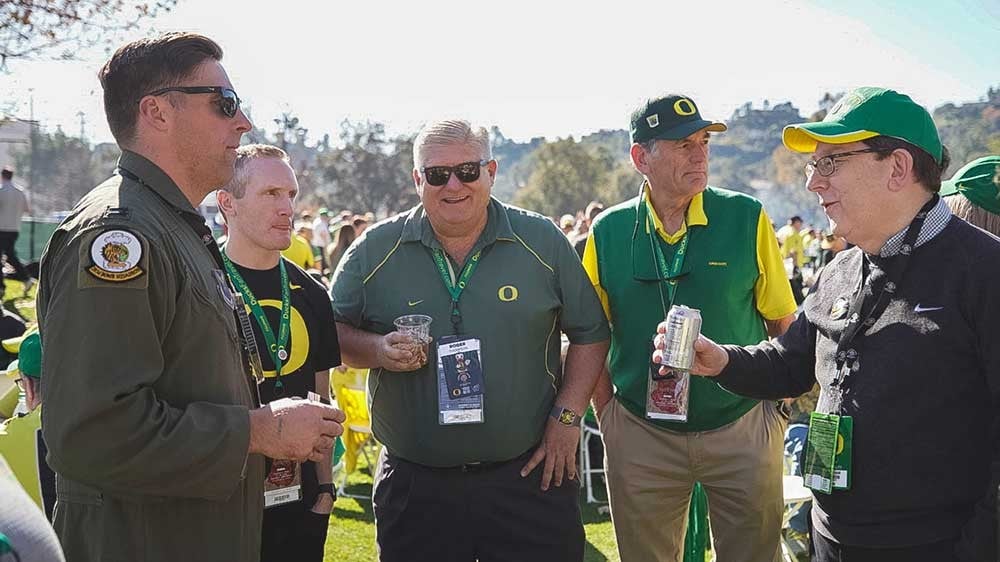 Michael Schill talking with Nick Reed, who is wearing his flight suit, at the UO Alumni tailgate