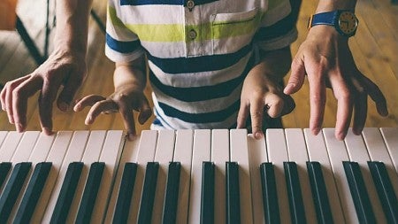 Adult's and child's hands working together to play a piano keyboard.