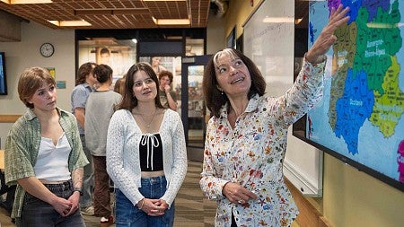 Female French teacher pointing to a map in front of two students