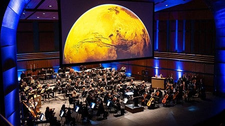 Bach festival symphony playing on stage in front of a large planet on a screen