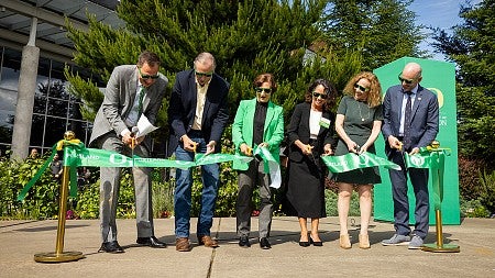 Three men and three women wearing green sunglasses and cutting a ribbon