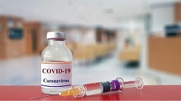 COVID-19 vaccine in bottle with a syringe next to it.