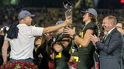Mario Cristobal, Justin Herbert, and Rob Mullins on the stage with the Rose Bowl trophy during the trophy presentation