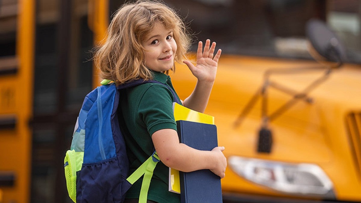 A young child waving goodbye as he gets on the schoolbus