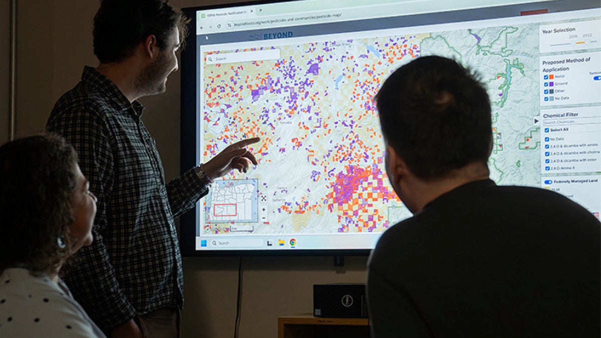 three researchers look at a pesticide application map on a large screen