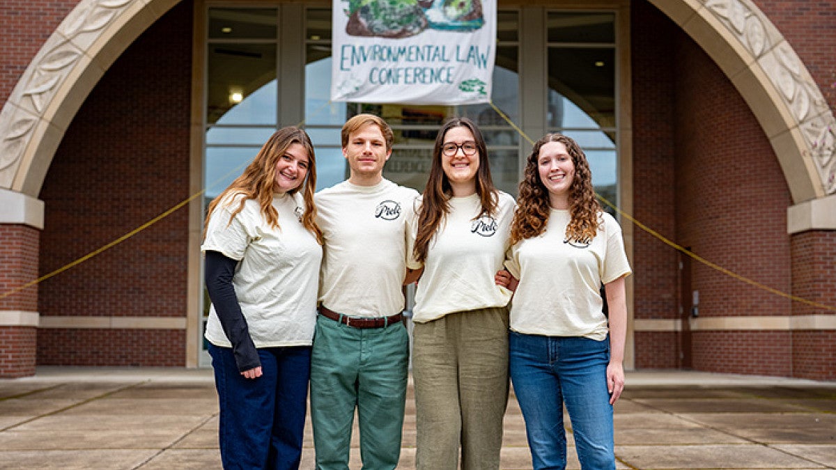 four students standing in front of an Environmental Law Conference banner