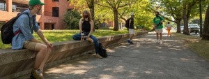 Two students sitting 6 feet apart outside Oregon Hall on a bench while wearing masks